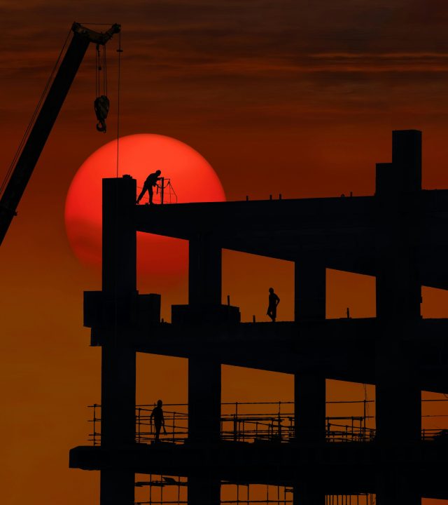 Silhouette of a construction site with workers against a dramatic sunset backdrop.